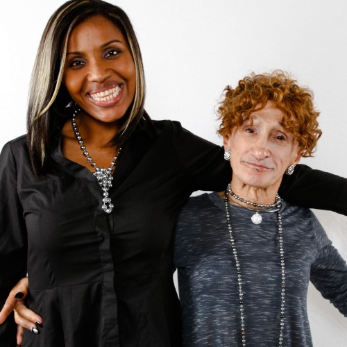 Two people stand next to each other, arms around eachother, smiling at the camera