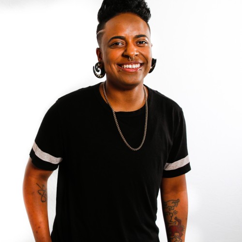 Person in black t-shirt, smiling at the camera with arms relaxed at side.